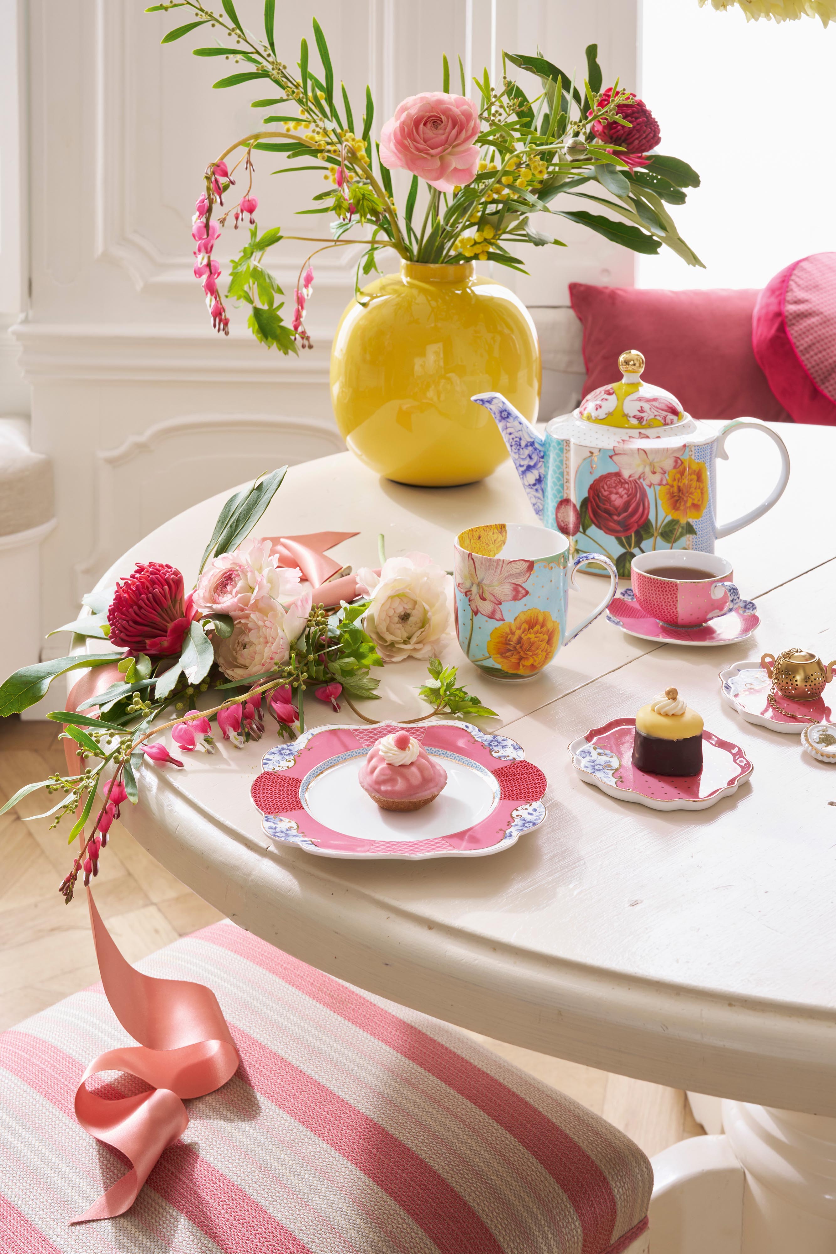 Pip Studio Royal Multi konvice, hrnek s podšálkem barevné růžové, talíř barevný růžový, miska barevná růžová , žlutá váza s květinami.